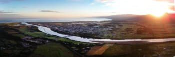 Aerial view of a town and surrounding farmland at sunset with a river winding toward the coast.