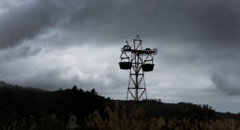 A silhouetted mining structure stands in a field of tall grasses against a cloudy sky on a hillside.