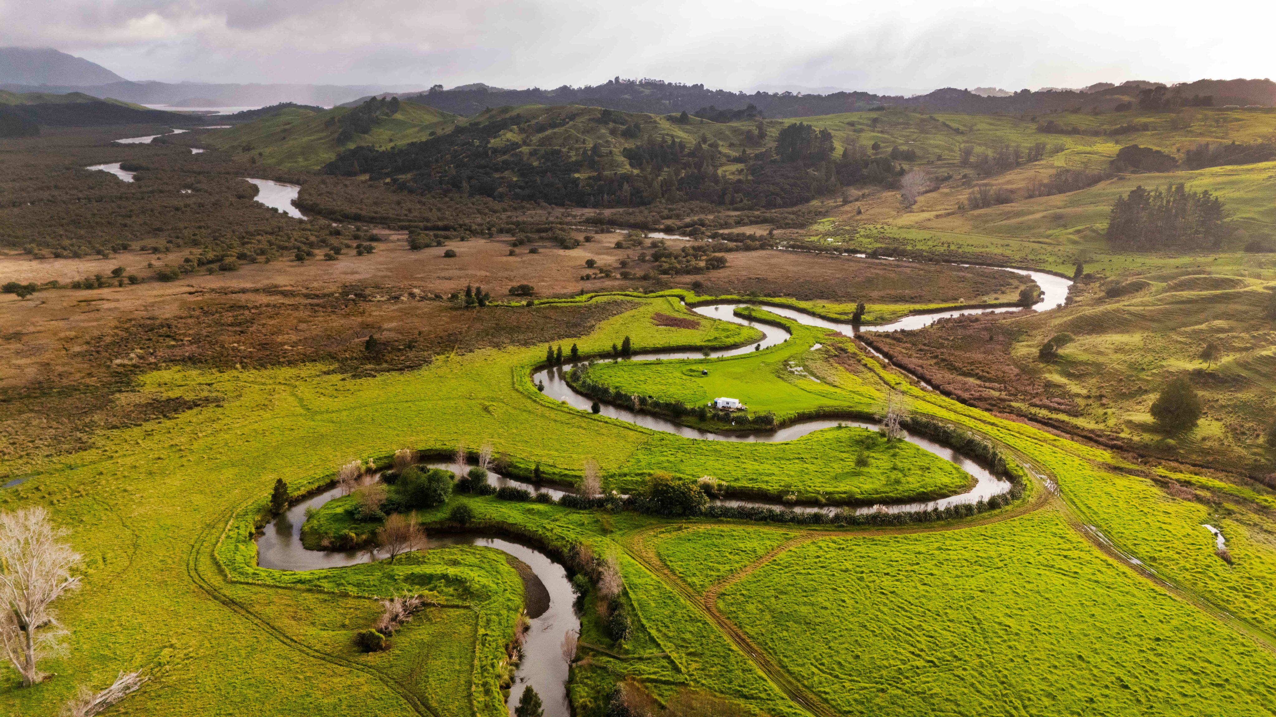 Wide view of river valley, with channel twisting back and forth across paddocks and wetlands.