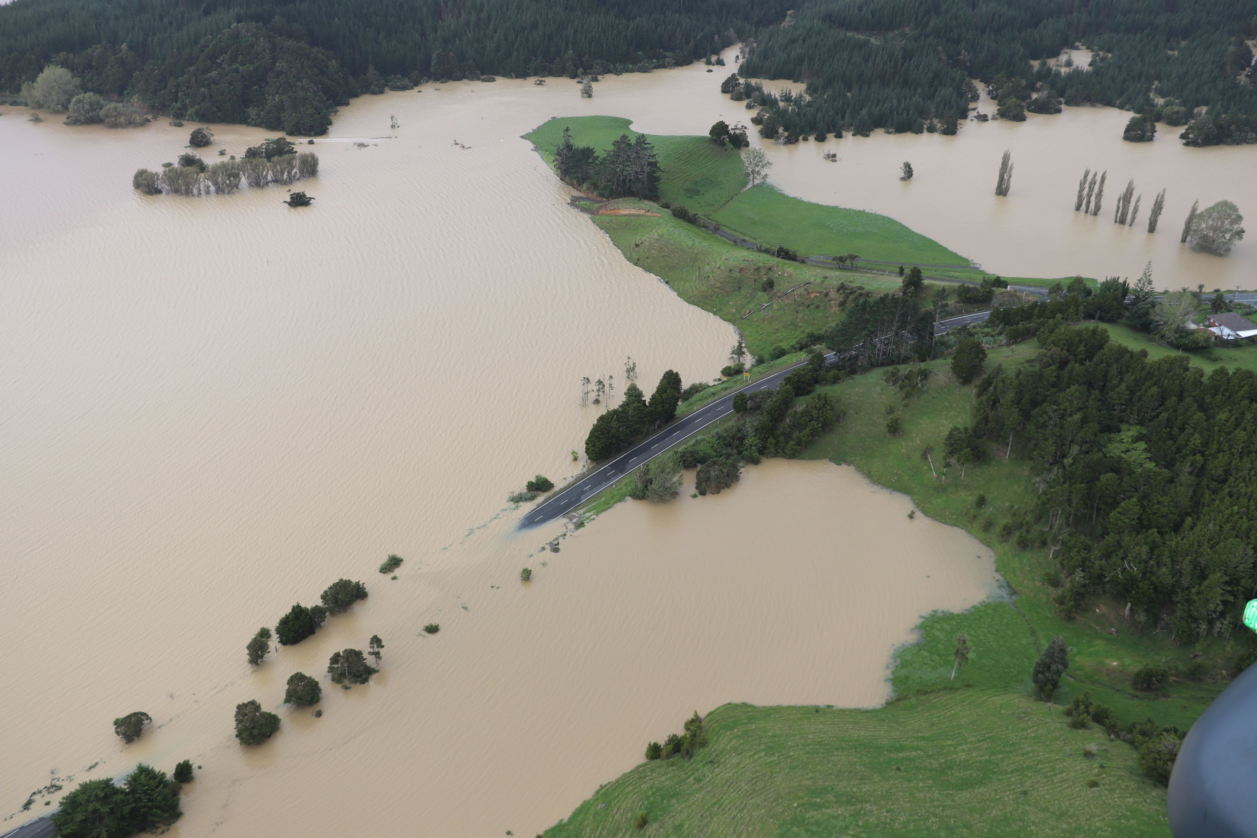 Aerial view of deep floodwaters, road on hillside dropping under brown water. 