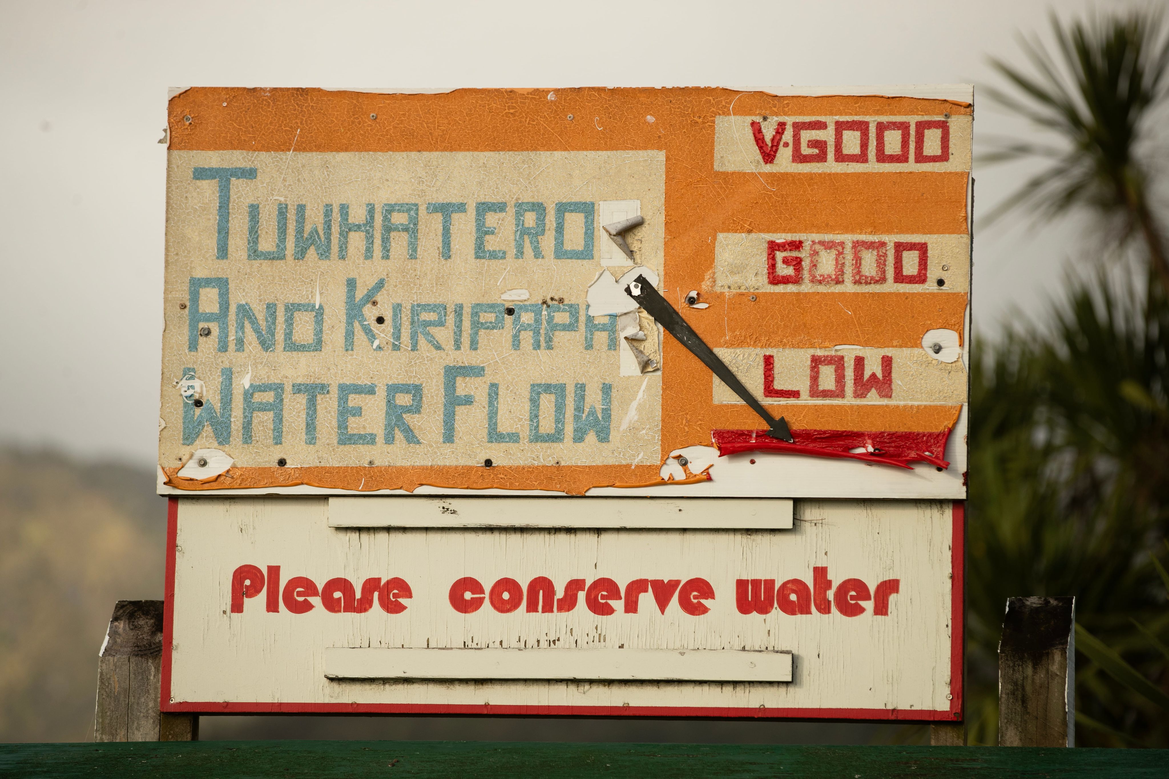 A weatherbeaten sign, with an arrow gauge pointing to a red zone below LOW and a headline 'Please conserve water'.