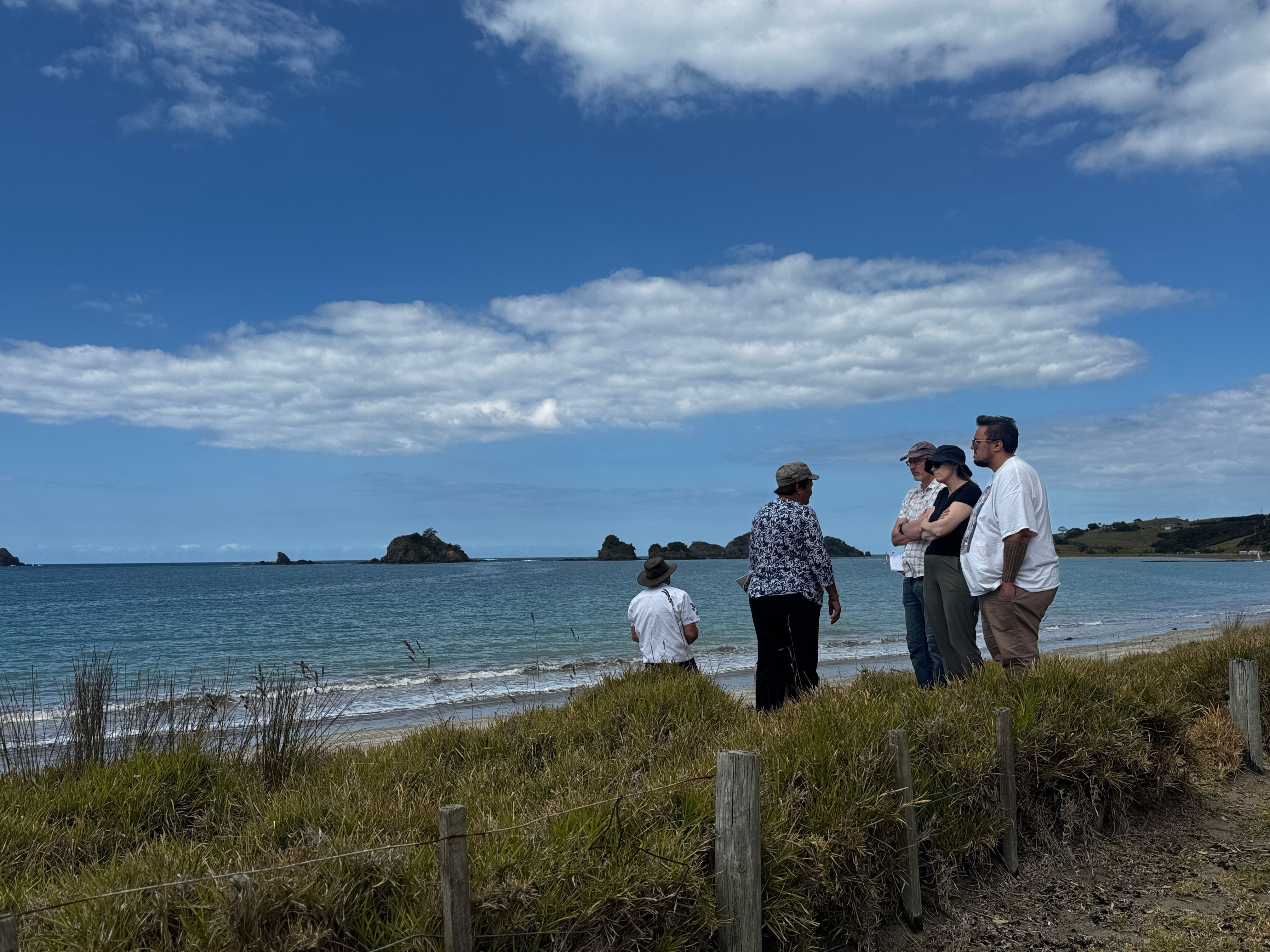 Five people standing on sand dunes in a sweeping bay under a blue sky. 